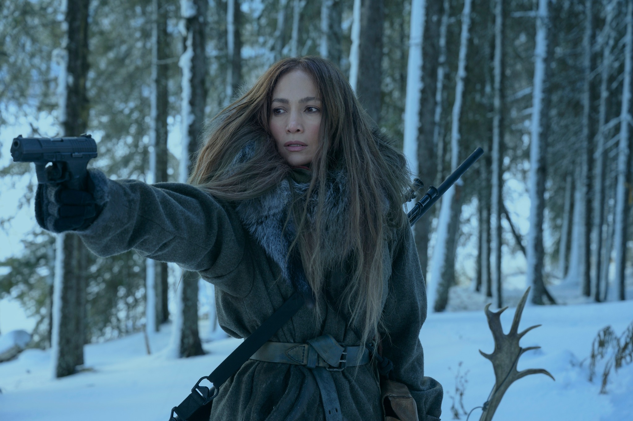 Jennifer Lopez stands in the snowy woods pointing a gun in the film The Mother