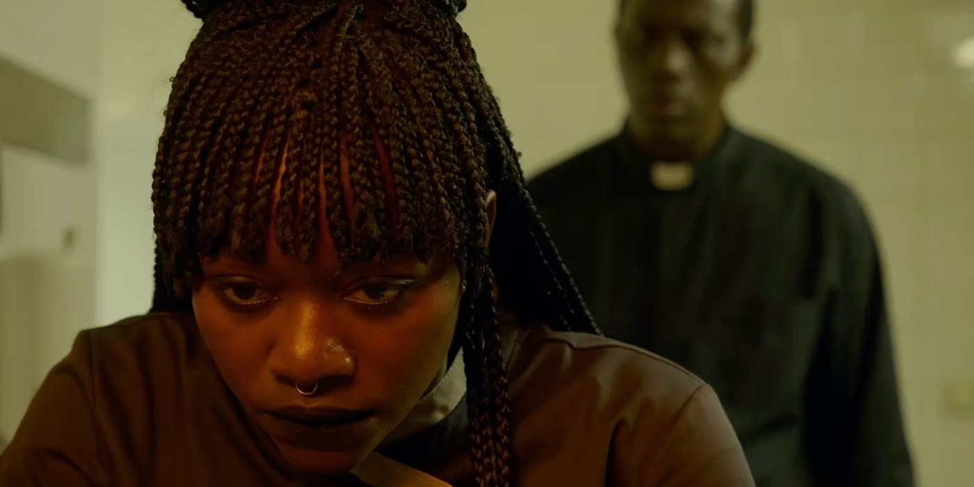 Souleymane Sy Savane plays Father Patrick, a priest standing creepily behind Marie played by Babetida Sadjo Babetida Sadjo in the film Our Father, The Devil.